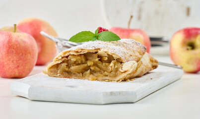Baked strudel with apples sprinkled with powdered sugar on a white wooden board