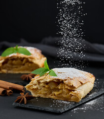 Baked strudel with apples sprinkled with powdered sugar on a black board