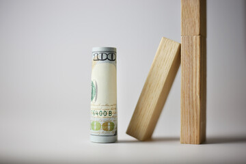 A rolled up 100 dollar bill stands next to wooden cubes on a light background. Currency concept
