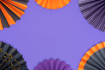 Halloween background. Bright paper fans are laid out in the form of a frame on a purple background. Purple, orange and black decorated paper fans as Halloween decoration with copy space.