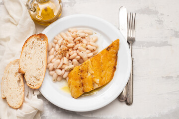 Fried cod fish with white beans on the plate.