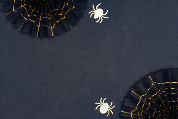 Golden spider and cobweb on a dark background with copy space. Scary Halloween shiny spiders and black paper fans with golden cobwebs. Halloween decorations on a black textured backdrop.