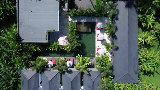 Small hotel with swimming pool, top-down aerial shot, green plants around. Camera fly up, reveal surroundings of modern accommodation at undeveloped place of the village at northwestern Bali