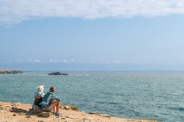 A couple of friends with white hair enjoy the view of the cliff as they sit. Cape Pen-Hir. Natural site in Camaret-sur-Mer.