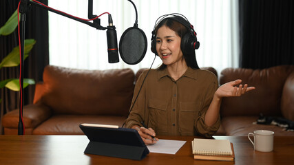 Young woman using condenser microphone and headphones to recording podcast in small home studio