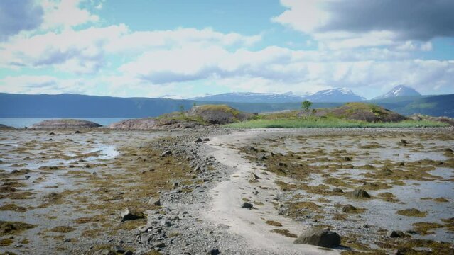 Drone following a beautiful reef leading to a small island with mountains in the background