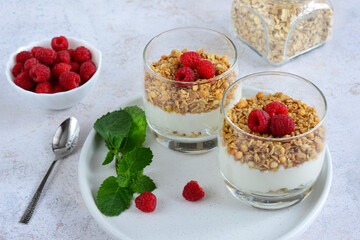 dessert with raspberry, muesli and yoghurt in drinking glasses on tray, close-up