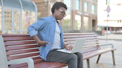 Young African Man with Back Pain Using Laptop while Sitting Outdoor on Bench