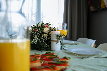 in a bright room, with daylight, a decorated festive table, with plates of food and glasses of orange juice