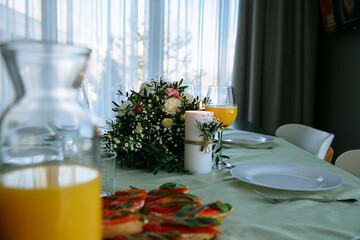 in a bright room, with daylight, a decorated festive table, with plates of food and glasses of orange juice