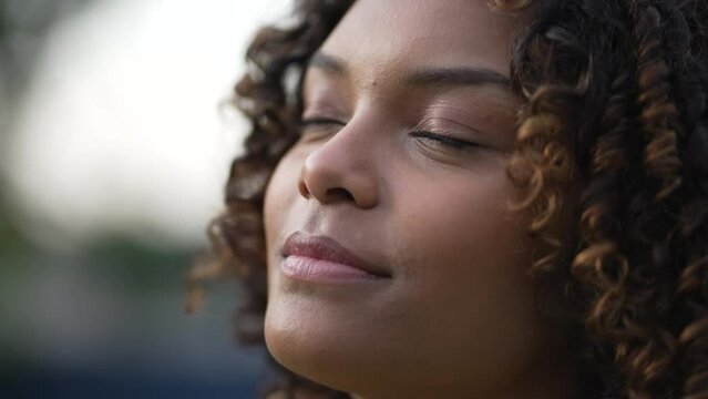 Meditative African American young woman closing eyes in contemplation. A black millennial girl opening eye smiling feeling grateful