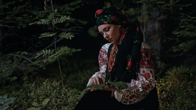 Witch woman in traditional ukrainian handkerchief and costume collects herbs, ferns at night in Carpathian mountains forest. National dress - vyshyvanka, ancient coral beads. Folk medicine concept.
