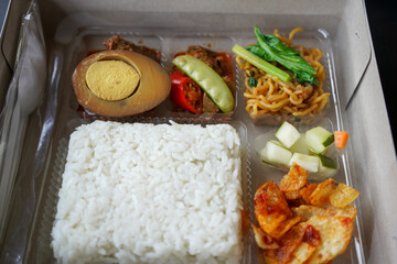 Serving rice boxes in white boxes from cardboard or paper boxes. White rice, potato fried chili sauce, pickled cucumber, vegetables, egg bacem, beefsteak beef rendang. Potato chips, chili paste. 