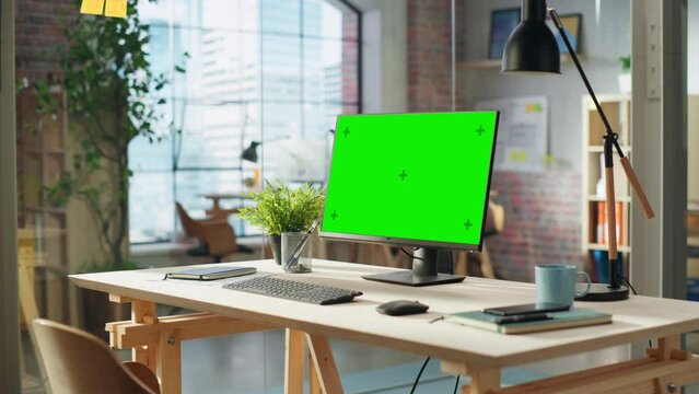Establishing Shot: Desktop Computer Monitor with Green Screen Mock Up Chroma Key Display Standing on a Desk in Modern Creative Office. Cozy Agency Space in Loft Building.