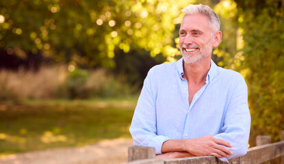Fototapeta premium Casually Dressed Mature Man Leaning On Fence On Walk In Countryside