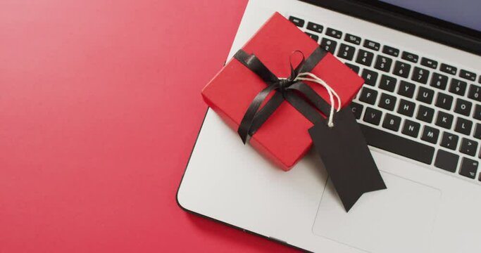 Laptop and red gift box with black ribbon and gift tag, on red background with copy space