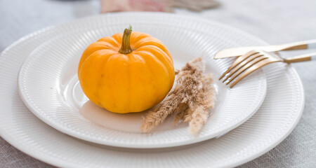 Beautiful autumn table setting. A plate with a cotton napkin and pumpkins. Table gold and a vase with autumn flowers on a linen tablecloth. The concept of festive serving for Thanksgiving.