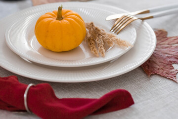 Beautiful autumn table setting. A plate with a cotton napkin and pumpkins. Table gold and a vase with autumn flowers on a linen tablecloth. The concept of festive serving for Thanksgiving.