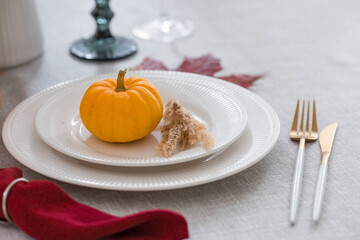 Beautiful autumn table setting. A plate with a cotton napkin and pumpkins. Table gold and a vase with autumn flowers on a linen tablecloth. The concept of festive serving for Thanksgiving.