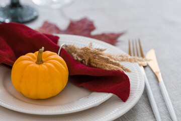 Beautiful autumn table setting. A plate with a cotton napkin and pumpkins. Table gold and a vase with autumn flowers on a linen tablecloth. The concept of festive serving for Thanksgiving.