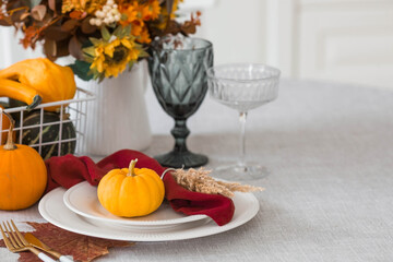 Beautiful autumn table setting. A plate with a cotton napkin and pumpkins. Table gold and a vase with autumn flowers on a linen tablecloth. The concept of festive serving for Thanksgiving.