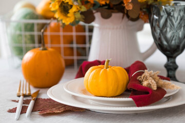 Beautiful autumn table setting. A plate with a cotton napkin and pumpkins. Table gold and a vase with autumn flowers on a linen tablecloth. The concept of festive serving for Thanksgiving.