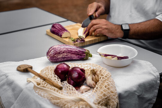 Mann sitzt am Tisch und schneidet Auberginen bei der Zubereitung einer Parmigiana di Melanzane