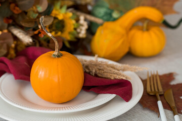 Beautiful autumn table setting. A plate with a cotton napkin and pumpkins. Table gold and a vase with autumn flowers on a linen tablecloth. The concept of festive serving for Thanksgiving.