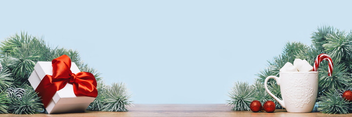 white gift box with a red ribbon bow with Christmas tree branch. Baubles. Hot chocolate mug with marshmallow. Christmas and New Year banner. Copy space side view