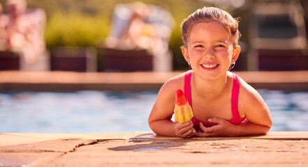 Portrait Of Family On Summer Holiday With Girl Eating Ice Lolly At Edge Of Swimming Pool