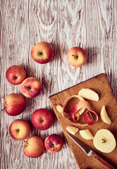 Juicy red apples and a curl of apple peel lying on a wooden table, stylized, top view