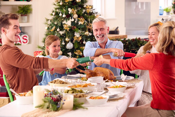 Multi-Generation Family Celebrating Christmas At Home Pulling Crackers Before Eating Meal Together
