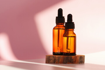 Banner of two transparent amber glass dropper bottles on pink background in the sunlight. Wooden podium. Pipette with fluid hyaluronic acid, serum, retinol. Cosmetics, healthcare, beauty 