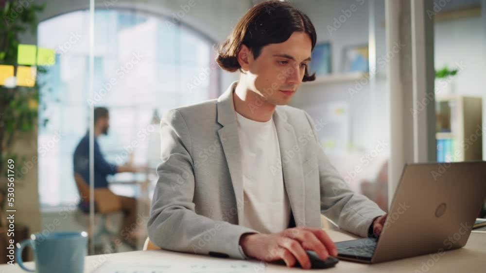 Poster handsome long-haired employee sitting at a desk in creative agency. stylish man using laptop compute