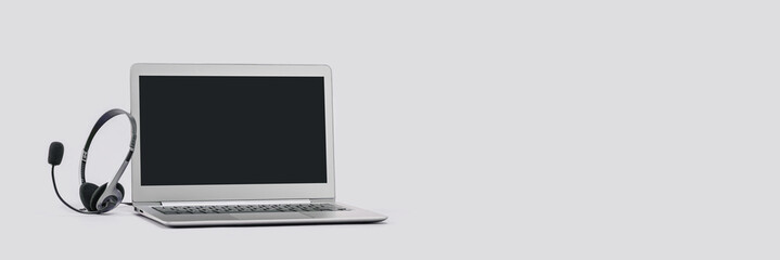 Front view of slim laptop with headset on grey. Monochrome background. Distant learning. working from home, online courses or support. Audio podcast headphones . Helpdesk or call center banner