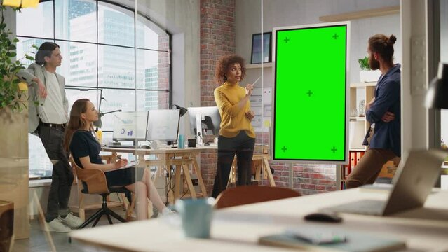 Driven Visionary Businesswoman Leading a Team Meeting in Creative Office Conference Room. Excited Multiethnic Female Showing Presentation on Green Screen Mock Up Chroma Key Monitor.