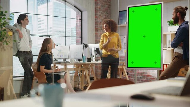 Excited Marketing Manager Leading a Team Meeting in Creative Office Conference Room. Multiethnic Female Showing Project Plan Presentation on Green Screen Mock Up Chroma Key Monitor.