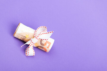 fifty euro banknote money roll tied with a white gift ribbon isolated on a purple background