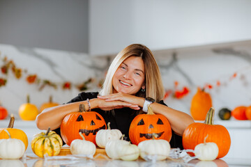 Woman posing with coloured pumpkins for halloween on white kitchen.