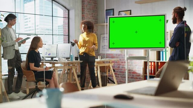 Excited Business Coach Making a Presentation for a Young Perspective Team in Creative Office Conference Room. Multiethnic Female Showing Slides on Green Screen Mock Up Chroma Key Display. Static Shot.