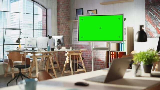 Empty Conference Room for Team Meetings in Modern Creative Agency with Art on Walls and Desks with Computers. Office Space with Digital Green Screen Mock Up Chroma Key Monitor for Presentations.