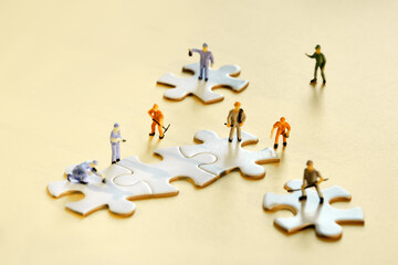 Team of tiny worker miniature figures on linked jigsaw puzzle pieces on golden yellow paper....