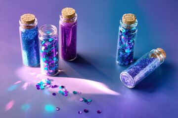 Glitter products in transparent bottles, close-up. Various glitter powrer and particles in neon...