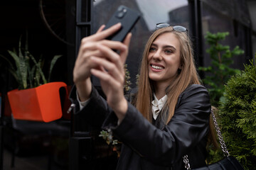 Fototapeta na wymiar young woman blogger takes a selfie next to a popular cafe in the city