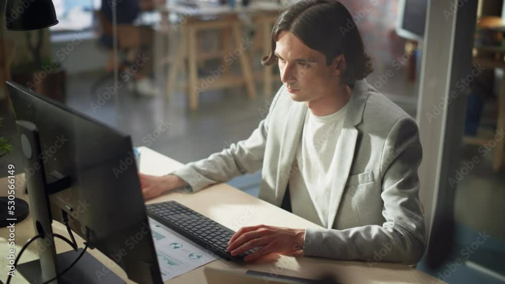 Poster stylish long-haired manager wearing a gray jacket, working at a desk in creative office. young hands