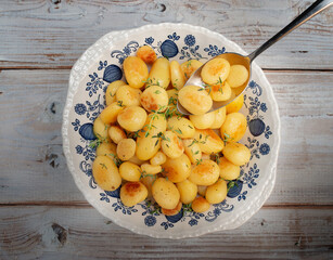 Roast baby potatoes garnished with thyme in rustic, blue and white serving dish