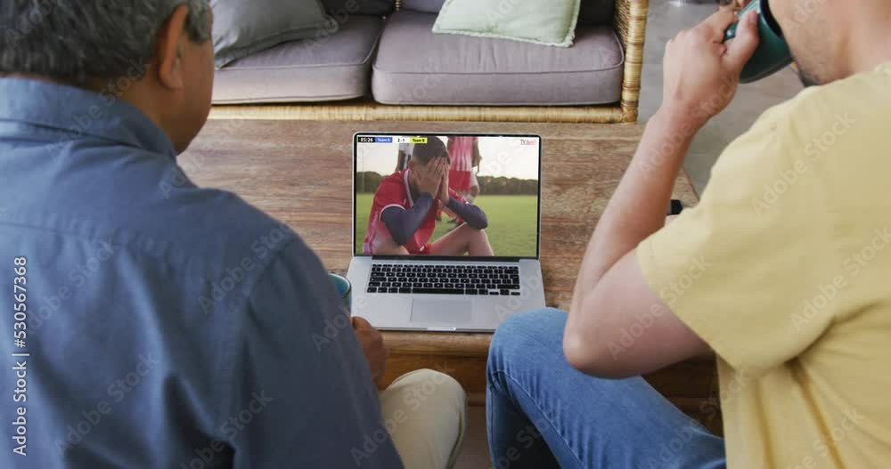 Poster Biracial father and son watching laptop with diverse male soccer players playing match on screen