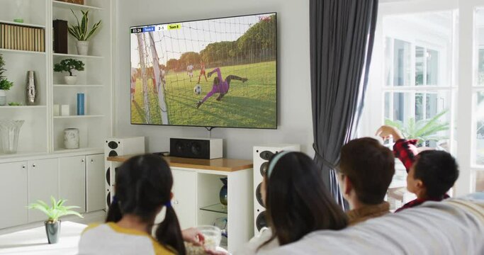 Asian Family Watching Tv With Diverse Male Soccer Players Playing Match On Screen