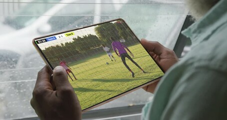 African american man using tablet with diverse male soccer players playing match on screen - Powered by Adobe