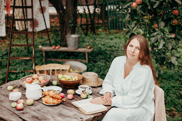 young woman model plus size in white dress sit at table with pet dog poodle, resting and drinking tea after harvesting autumn in back yard, fall and harvest, zero waste life, eco-friendly simple life